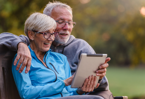 An elderly couple sits comfortably together, interacting with a tablet in their hands.